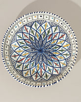A ceramic decorative large bowl with hand-painted patterns in blue, green, and other colors on a white background, displayed against a neutral backdrop.